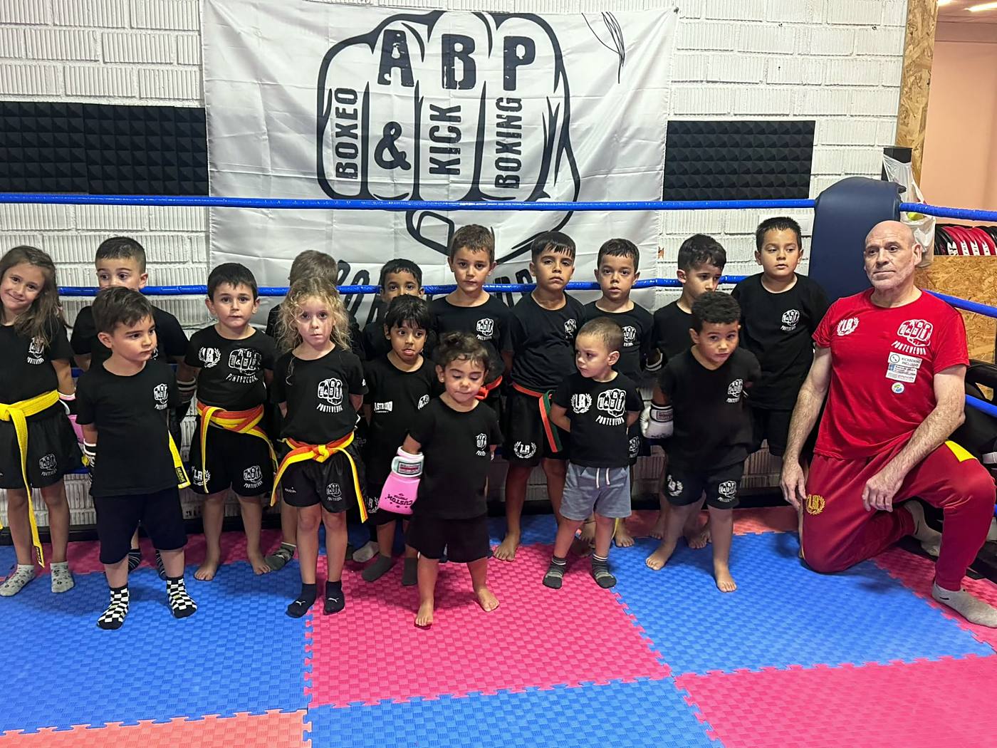 Grupo de niños y niñas de la clase infantil con su profesor delante del banner de ABP Sport