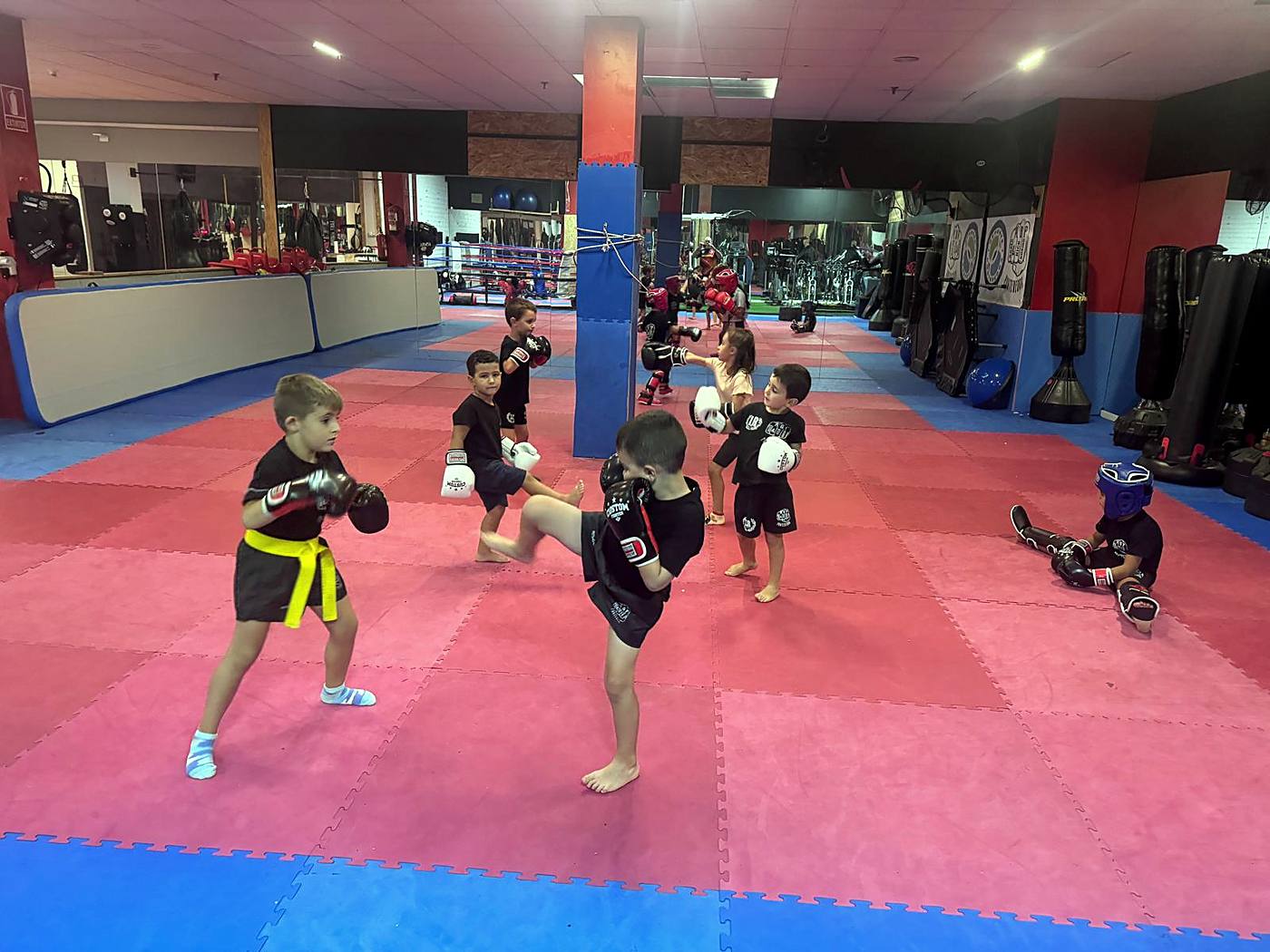 Niños con guantes practicando una patada de rodilla en la clase infantil de ABP Sport